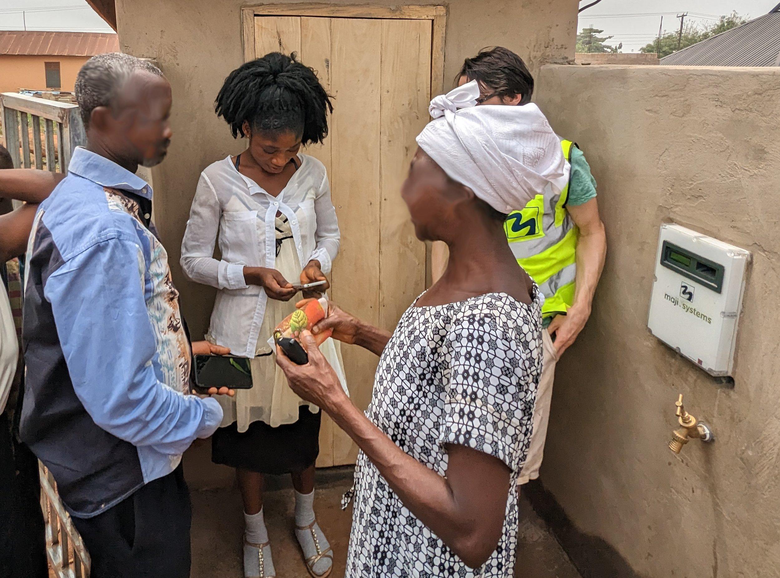 A reseller using the Maji Systems app on a phone to top up a customer’s WaterCard beside a dispenser