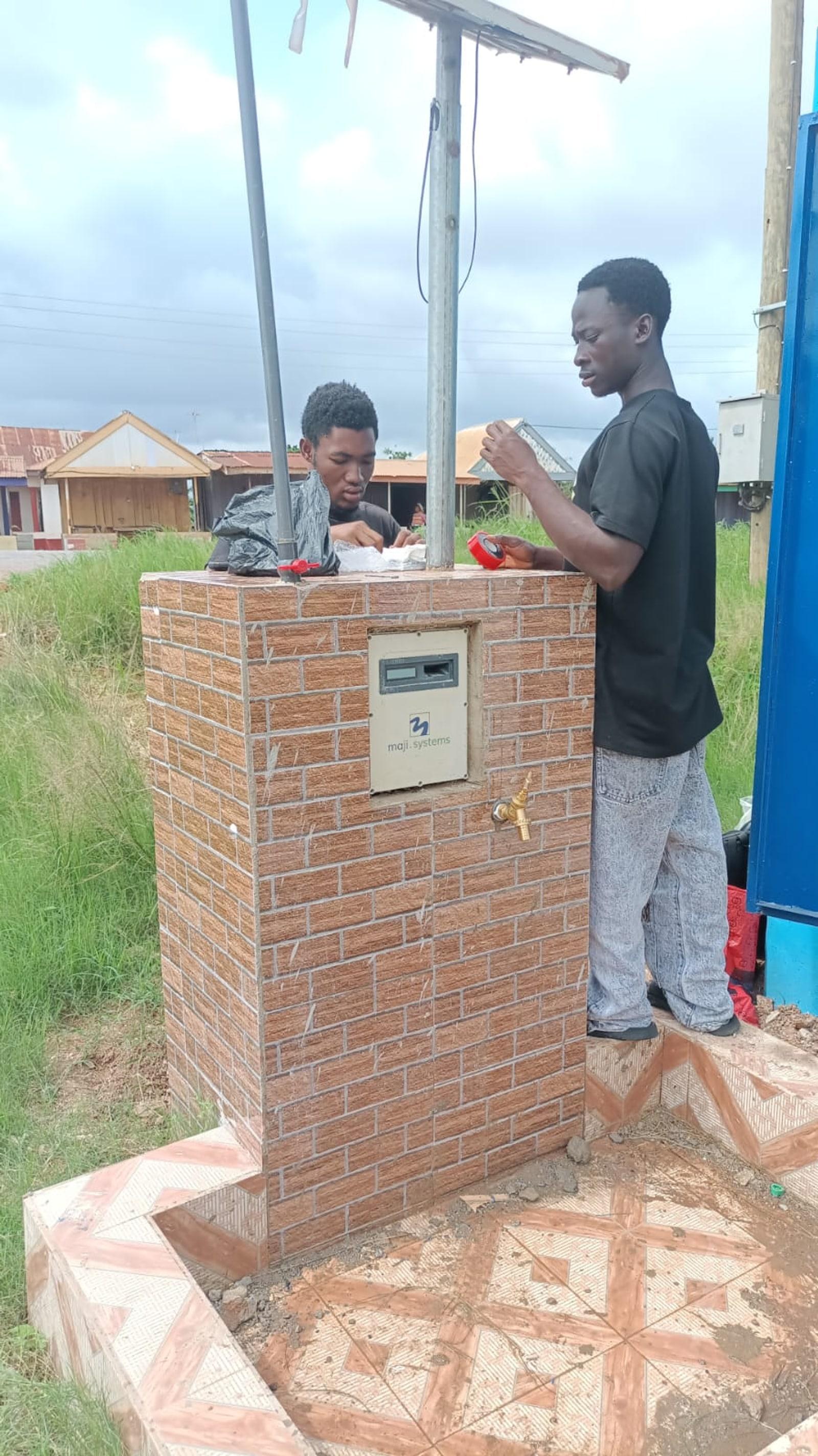 Two OM Water Systems installers fitting a Maji Community Dispenser onto a tiled standpipe in Kumasi, Ghana